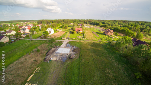 Aerial view on detached house under construction. House In foundation state. Located on green plot in small village. Wooden roof structure. Meadows around.