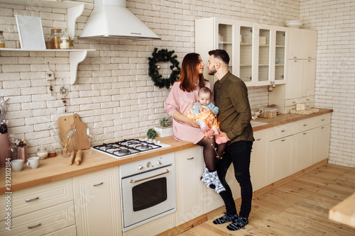 Beautiful young family with little daughter at the kitchen, decorate the house for Christmas celebration, happy parents with cute toddler spend winter holidays, xmas concept