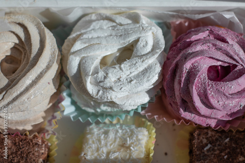 Sweet homemade dessert zephyr pink, beige, white - big marshmallows and 'bird milk' candies in a white gift box on a white table. handmade Big zephyr sprinkled with powdered sugar. Food photography