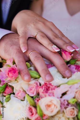 Hands of the engaged bride and groom lie on a bouquet