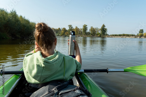 The girl in the boat holds a thermos for tea. Rafting down the river with a thermos. © vzwer