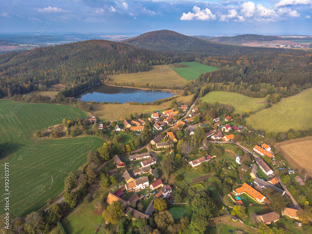 Aerial view of a small village hills in background.Top view of traditional housing estate in Czech.Houses from above, real estate concept.Countryside urban scene.Beautiful hilly landscape,pond,meadows