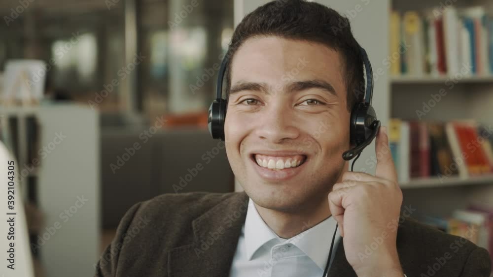mixed race man in office with headset smiling at camera, workplace support agent