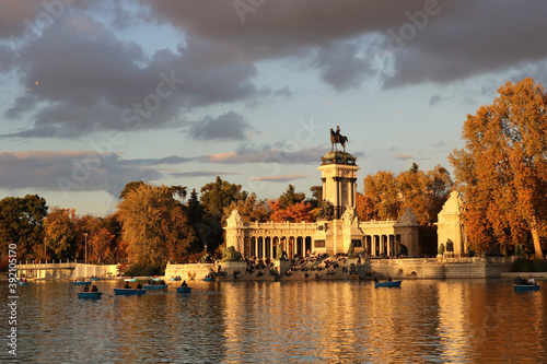 landscape of a lake with boats in the Retiro park of Madrid with the monument in the background and autumnal trees in a cloudy day photo