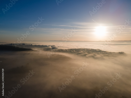 Aerial view of sunrise above foggy town. Mystical fog scattering sunrays of upcoming sun.