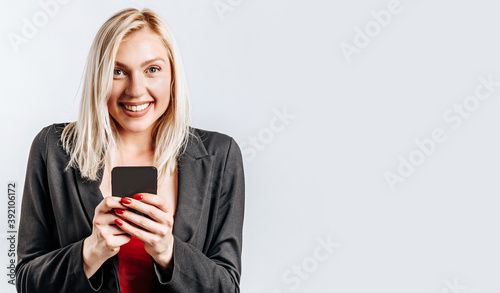 Beautiful young cute girl smiling and holding phone on gray isolated background