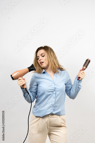 Photo of a woman on a light background. The girl is holding a hair hairdryer and a comb. The eyes are closed. High quality photo.