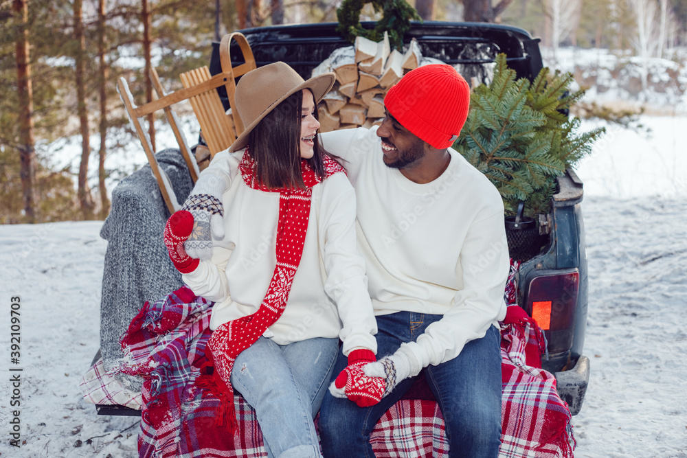 Obraz premium Happy multiracial couple in white sweatshirts during a trip to the forest for the christmas tree.
