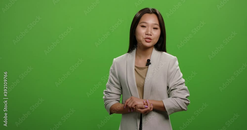 Positive asian woman looking at camera and talking during an advertisement. Female anchor during morning news report, shot on green background 4k footage Positive asian woman looking at camera and talking during an advertisement. Female anchor during morning news report, shot on green background 4k footage