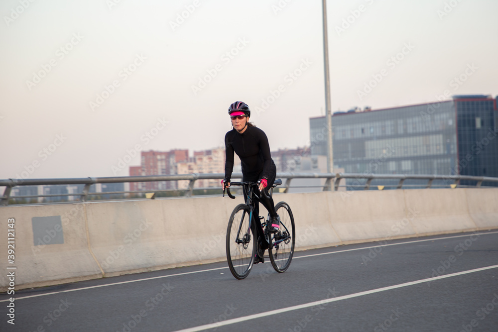 Obraz premium The girl rides a bicycle over the bridge. Morning workout in the city on a bike. Krestovsky Island St. Petersburg.