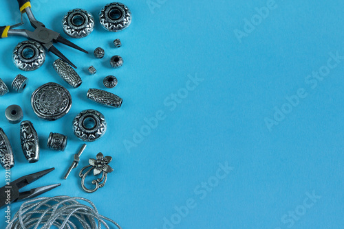 A set of silver accessories and tools for making jewelry on a blue background. Needlework.