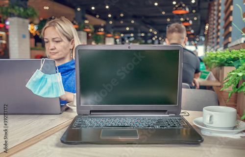 Woman sitting in cafe with laptop, laptop on foreground, copy space on the empty screen