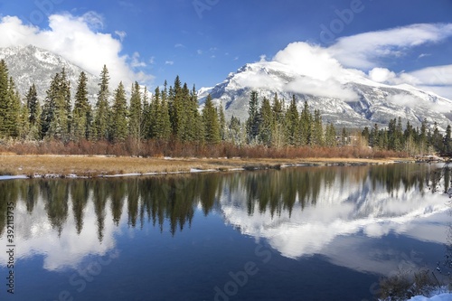 Snowy Mountain Peaks and Green Forest Trees Reflections in Blue Water of Spring Creek, Canmore Alberta, Canadian Rockies