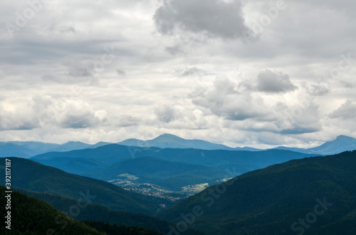 Landscape with forest, mountains and small Carpathian village in the valley under cloudy sky 
