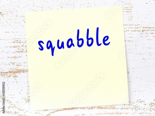 Yellow sticky note on wooden wall with handwritten word squabble photo