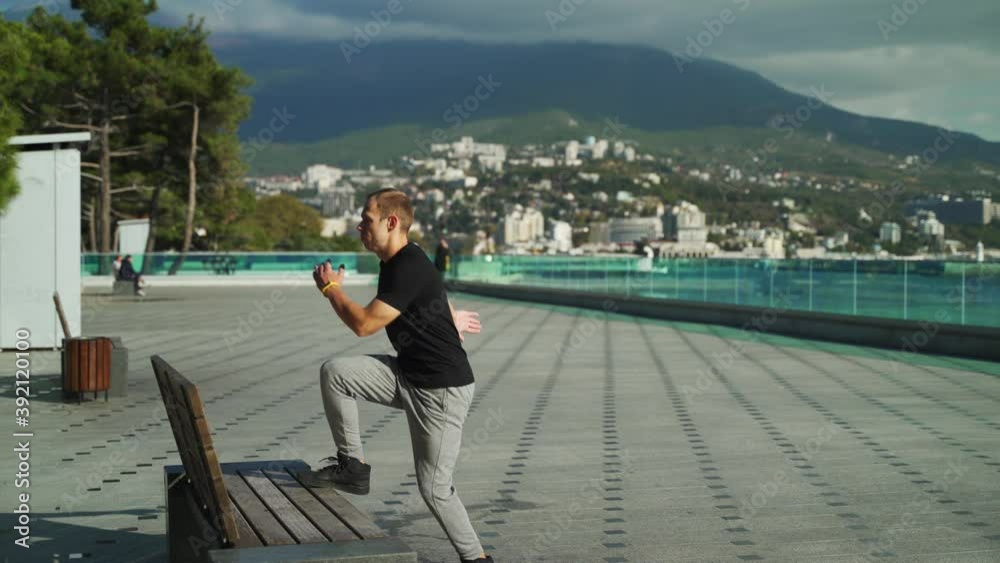 A young guy does morning exercises on a sunny day. A young man goes in for sports outdoors on the background of the sea. 4k A young guy does morning exercises on a sunny day. A young man goes in for sports outdoors on the background of the sea. 4k