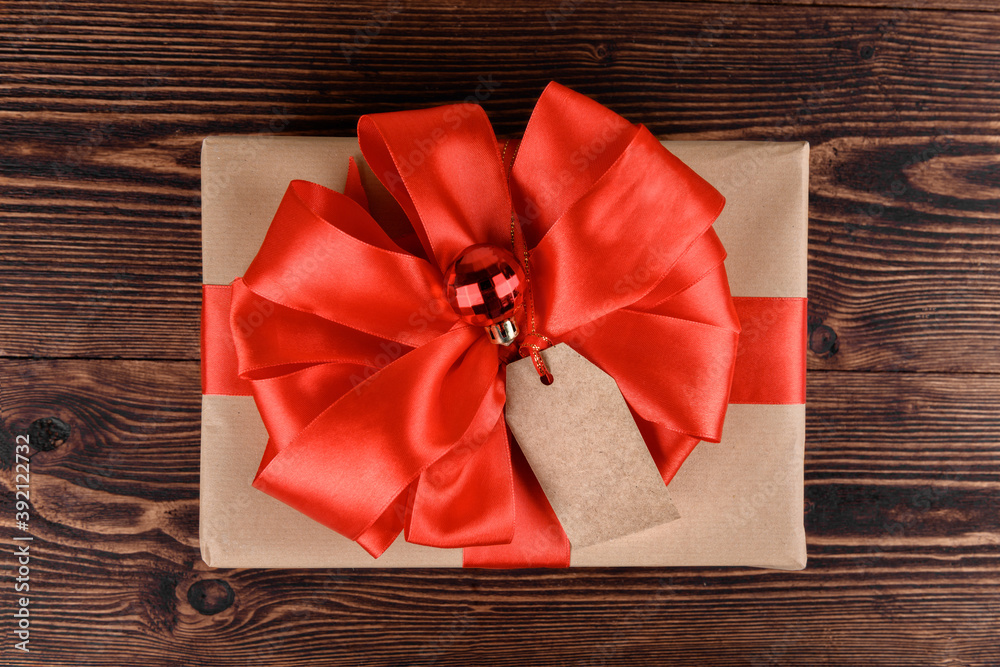 Gift box wrapped in recycled kraft paper with red ribbon bow and Christmas ball on a wooden background. Gift for Christmas or San Valentino, top view Gift box wrapped in recycled kraft paper with red ribbon bow and Christmas ball on a wooden background. Gift for Christmas or San Valentino, top view
