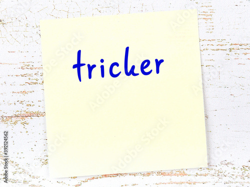 Yellow sticky note on wooden wall with handwritten word tricker photo