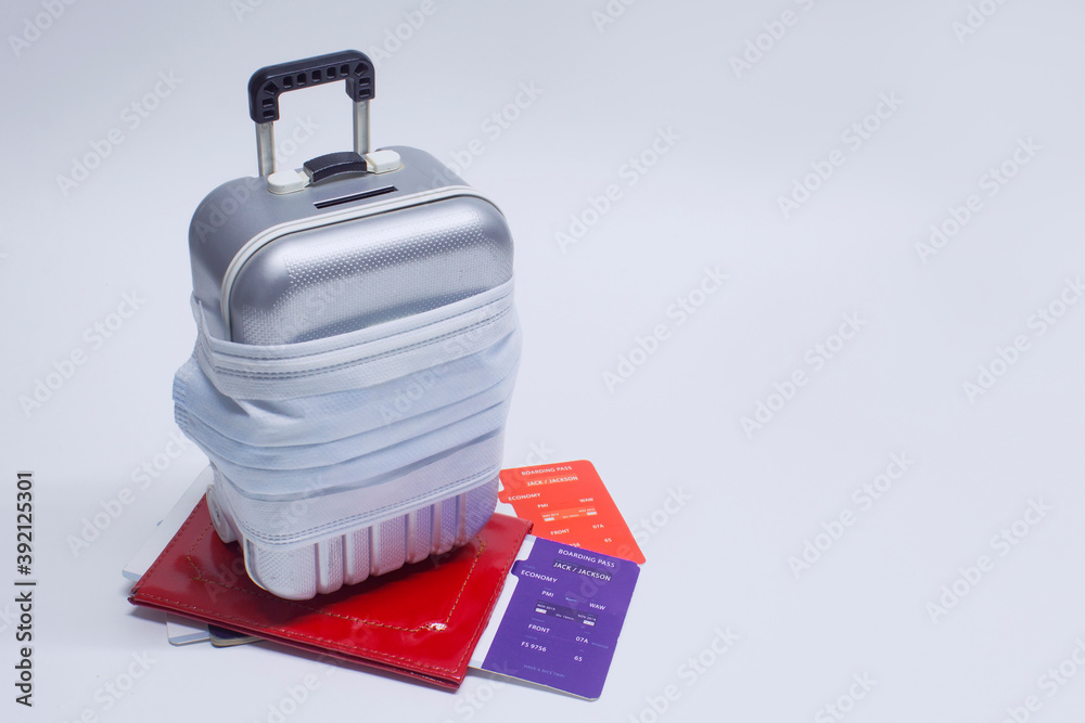 Obraz premium Time to travel. The concept of safe rest during a pandemic Covid-19 Coronavirus. Suitcase for travel with a medical mask and plane tickets with a passport.