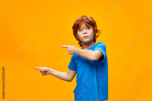 red-haired child in a blue t-shirt points his fingers to the side copy Space studio