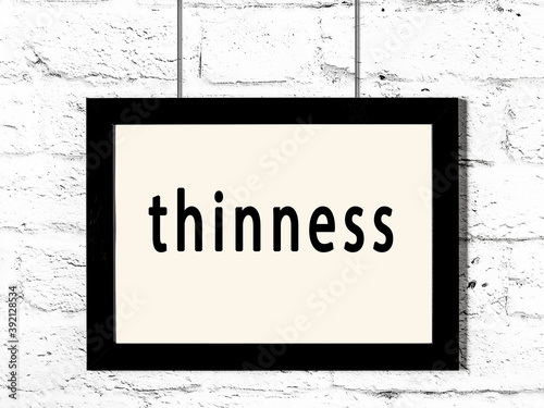 Black frame hanging on white brick wall with inscription thinness