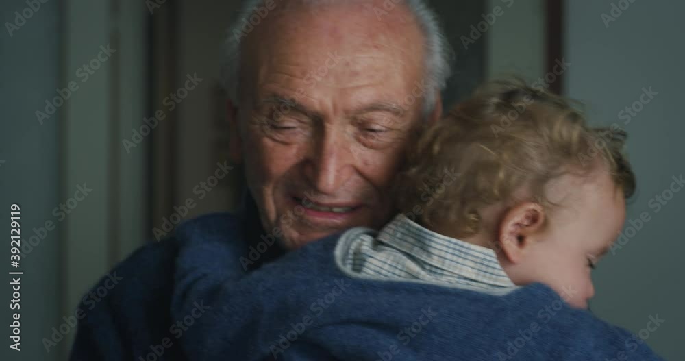 Cinematic shot of tender senior gray hair grandfather is cuddling a grandson baby while sleeping peacefully on  his arms at home.Concept of life, grandparents, love, care, generation, childhood