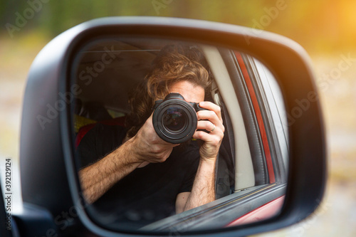 Handsome young traveler photographer taking photo from the car while driving on road trip. Concept about lifestyle, travel and people.