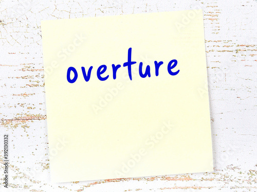 Yellow sticky note on wooden wall with handwritten word overture