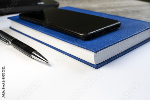 On a light background is a pen and Notepad with a black mobile phone. Business and training concept