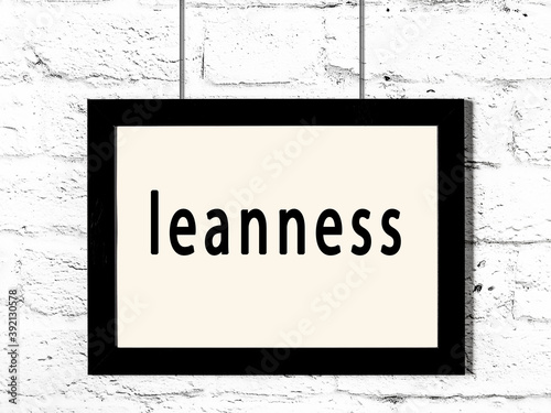 Black frame hanging on white brick wall with inscription leanness photo