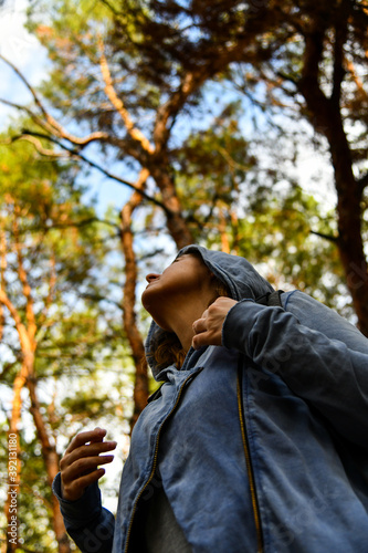 Tourist with a backpack and a hood at evergreen pine forest. Travel, ecotourism, ecology, local tourism concept, natural background with an explorer in hoodie and coniferous trees