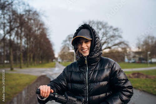 Woman in a jacket on an electric scooter in an autumn park. © teksomolika