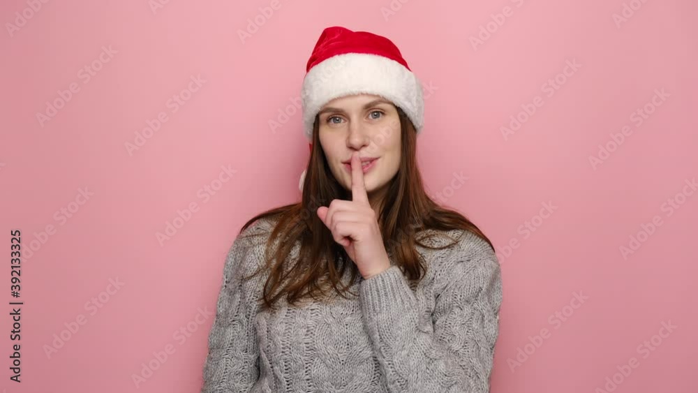 Secret woman look around say hush be quiet with finger on lips shhh gesture, dressed in cozy sweater and red Christmas hat, isolated on pink studio wall. New Year celebration merry holiday concept Secret woman look around say hush be quiet with finger on lips shhh gesture, dressed in cozy sweater and red Christmas hat, isolated on pink studio wall. New Year celebration merry holiday concept