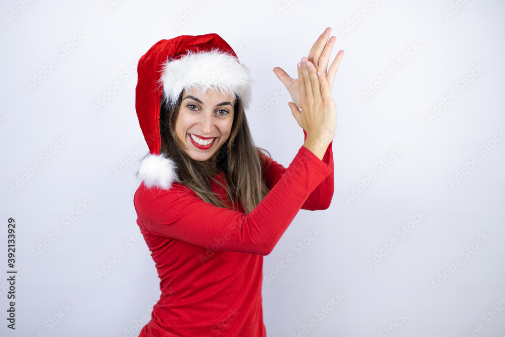 Young beautiful woman wearing a Santa hat over white background clapping and applauding happy and joyful, smiling proud hands together Young beautiful woman wearing a Santa hat over white background clapping and applauding happy and joyful, smiling proud hands together