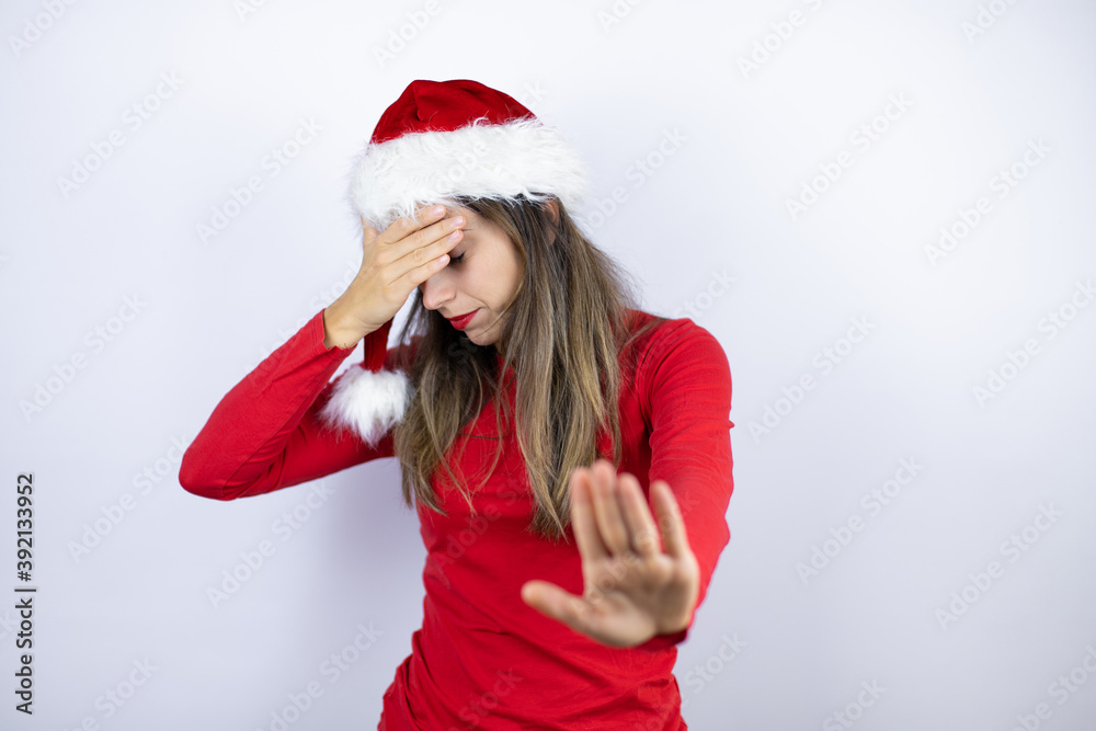 Young beautiful woman wearing a Santa hat over white background covering eyes with hands and doing stop gesture with sad and fear expression. Embarrassed and negative concept. Young beautiful woman wearing a Santa hat over white background covering eyes with hands and doing stop gesture with sad and fear expression. Embarrassed and negative concept.