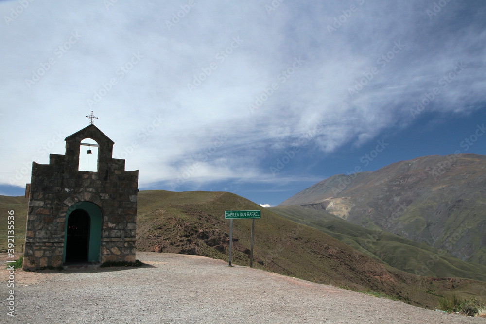 Small chapel made of stone very high in the popular landmark, Bishop's Slope in Salta, Argentina. The green mountains and sky with clouds in the background. 