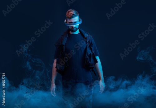 Young man on dark virtual reality background. Guy using VR helmet. Augmented reality, future technology, game concept. Blue neon light.