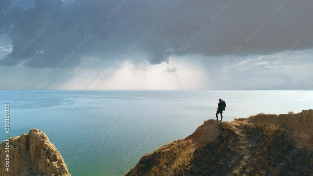 The tourist is standing on the mountain cliff on the seascape background