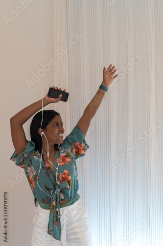 African woman with headphones listening to music from her smartphone and dancing at home