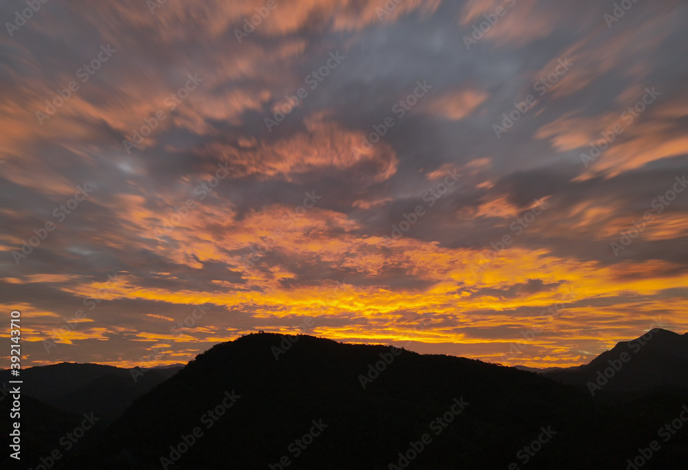 Sunset or sunrise sky with motion clouds in the sky above the silhouette mountains. aerial view by drone.
