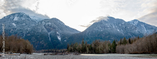 A beautiful panorama of mountains in British-Columbia with the Squamish River flowing in the foreground, autumn trees changing color, and a snow-line on the mountain