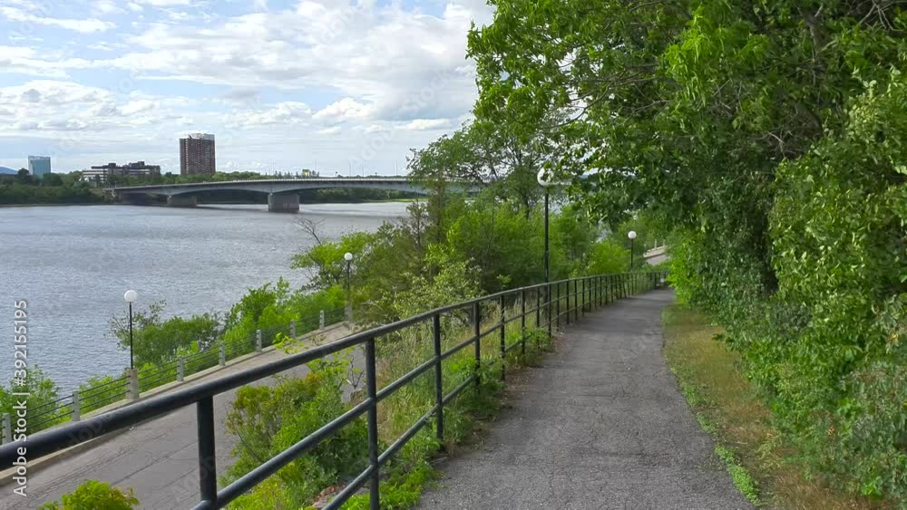 Walking and biking trail with view to street and river below plus bridge and buildings in background under blue sky in summer in Ottawa Ontario Canada Walking and biking trail with view to street and river below plus bridge and buildings in background under blue sky in summer in Ottawa Ontario Canada