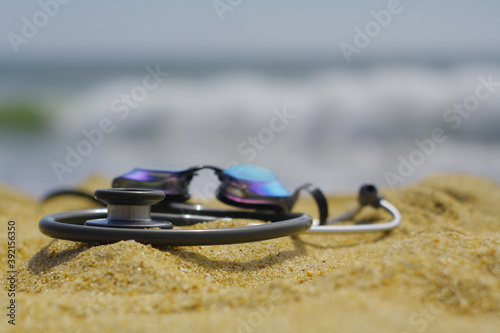 stethoscope lies on a beach with goggles on top of it to show that doctors need a break photo