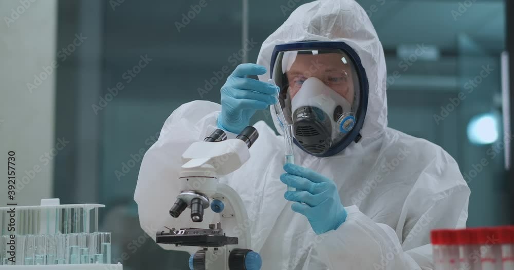 virologist is researching danger virus in laboratory, man is dressed protective overall and face mask with respirator, developing
