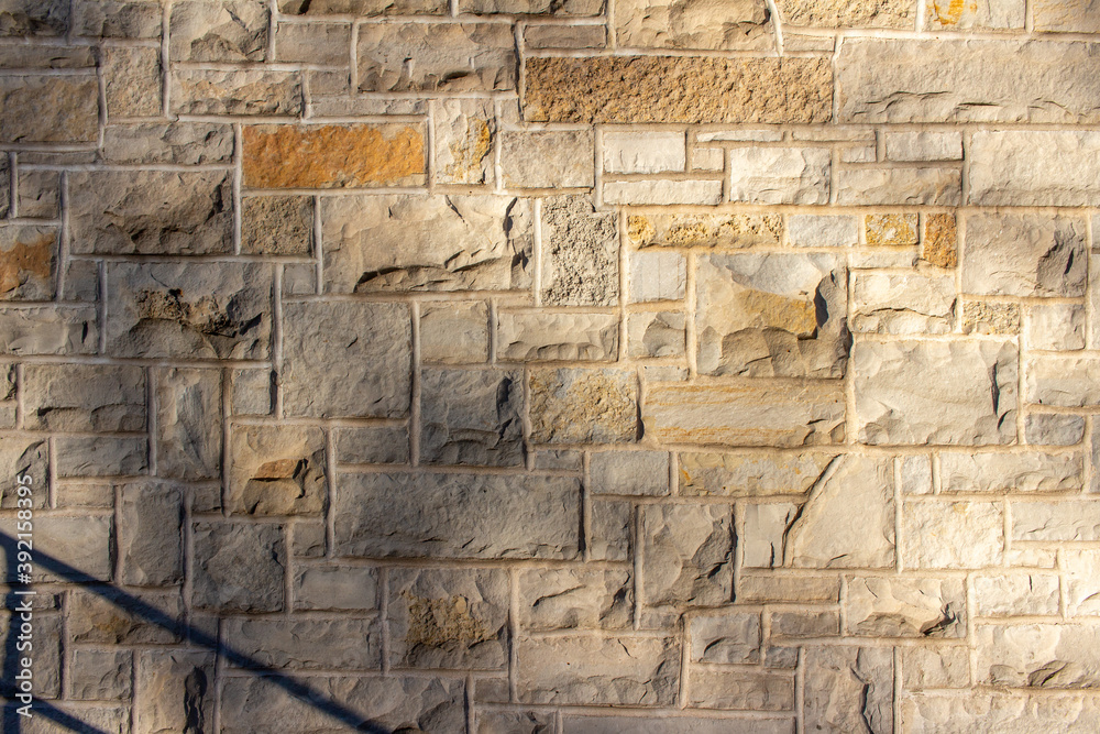 Full frame abstract background of an attractive tan brown natural limestone block wall in ashlar pattern, with rugged texture stone blocks in full sunlight with tree shadows and partial view of stairs