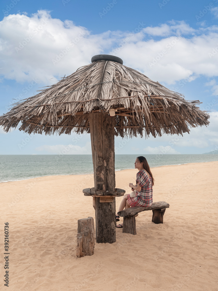 Asian woman sitting under straw umbrella on tropical beach. female looking to sea view.