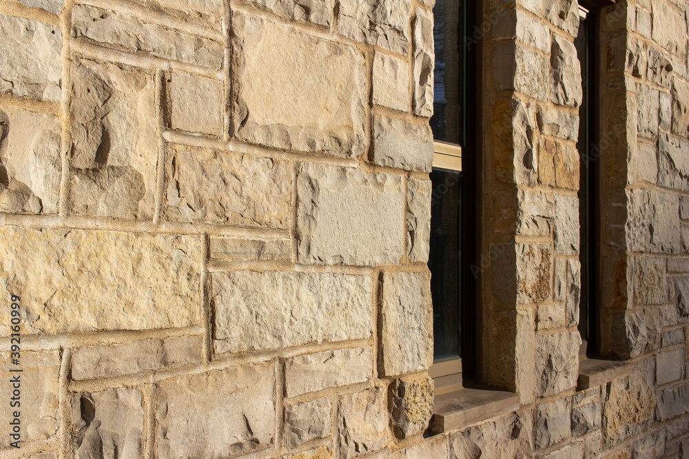 Full frame abstract background of an attractive tan brown natural limestone block wall in ashlar pattern, with rugged texture stone blocks in full sunlight, with partial view of windows and copy space