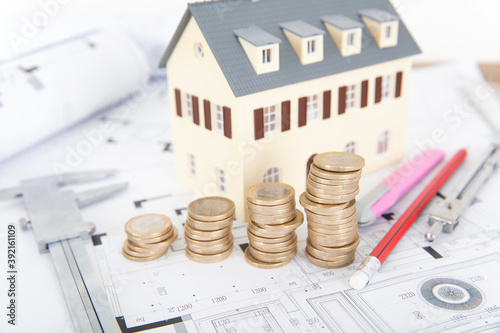 Interior design engineering drawings and small house model with a row of euro coins and related tools