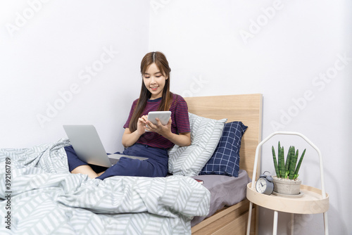 Asian woman working with smartphone or tablet on bed at home, Social media, stay home and quarantine or remote work and creativity concept.