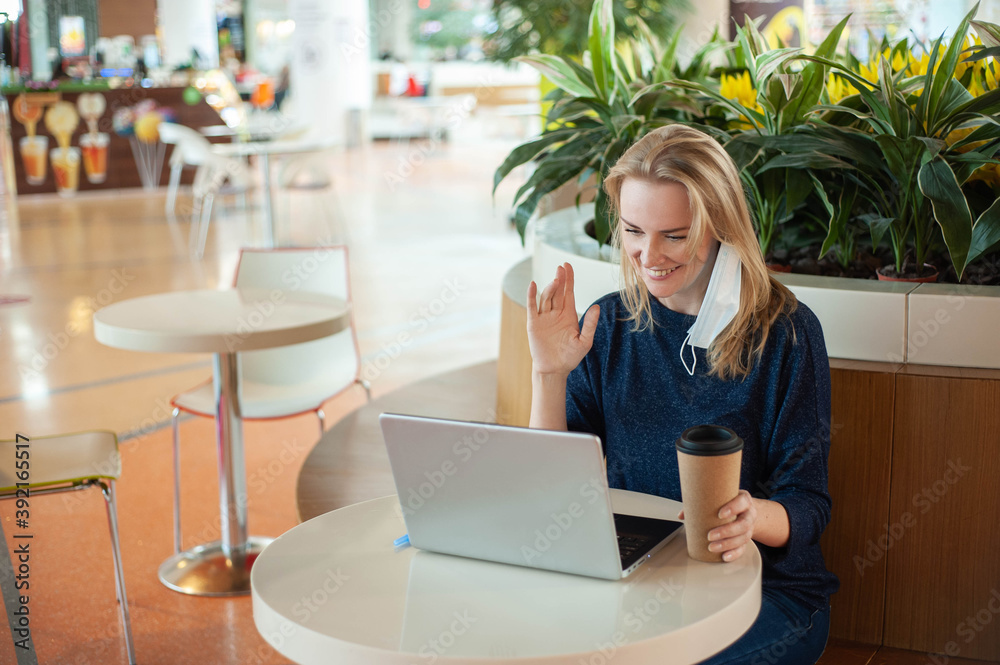 Study and work during the epidemic. Social distance. A blonde woman sit at a table in an empty cafe. A woman drinks coffee and communicates online with a laptop. Study and work during the epidemic. Social distance. A blonde woman sit at a table in an empty cafe. A woman drinks coffee and communicates online with a laptop.